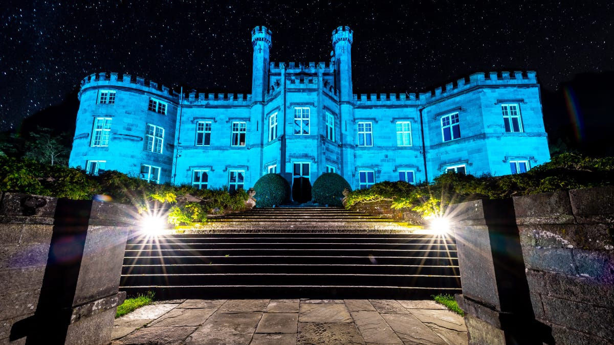 Bolesworth Castle illuminated in blue at night, with a starry sky in the background and dramatic lighting on the pathway.