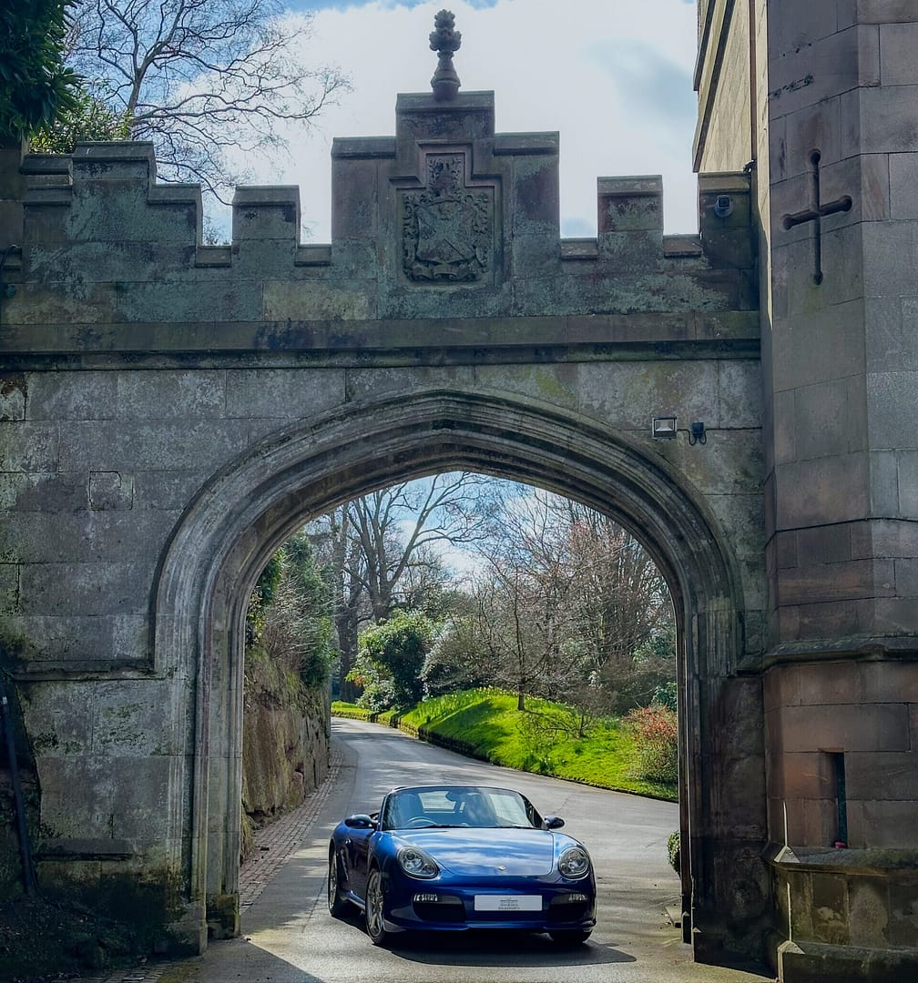 A blue Porche supercar parked under the historic and ornate stone archway at Bolesworth Castle