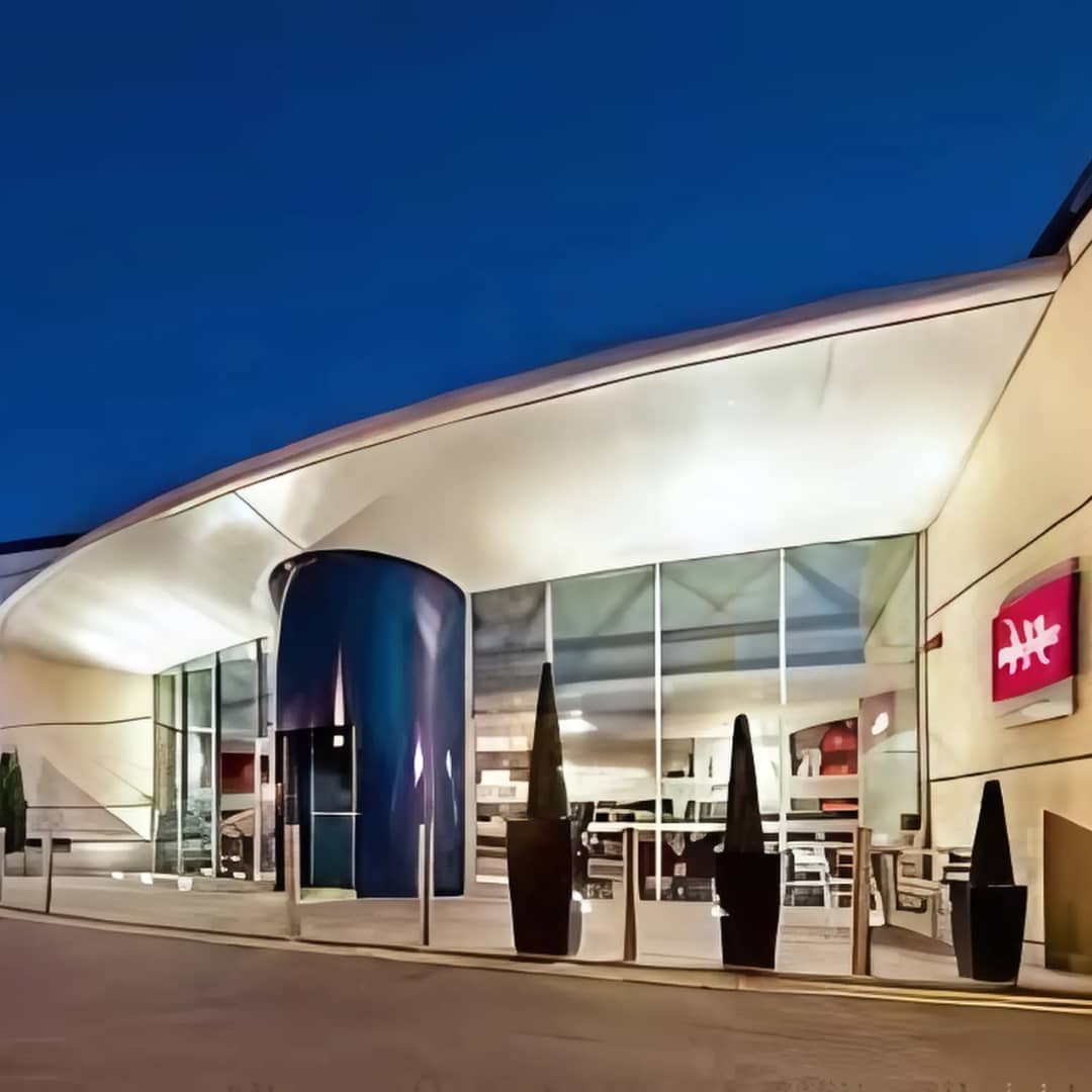 The Mercure Chester Abbots Well Hotel exterior at dusk, showcasing its modern curved entrance, glass façade, and ambient lighting, located near Chester city centre.
