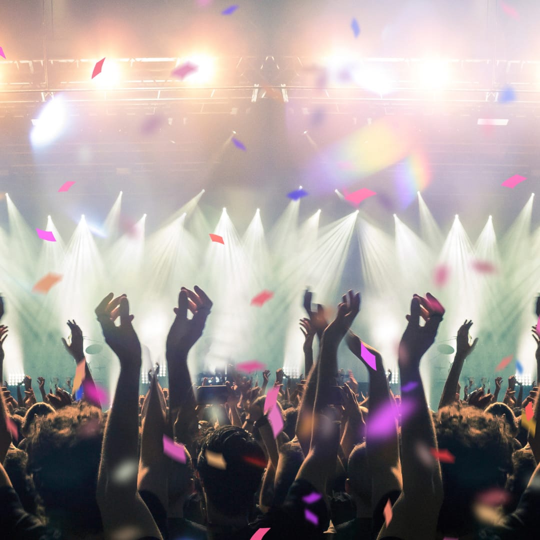 A vibrant festival crowd raising their hands in excitement as bright stage lights shine down, with confetti filling the air at the Together Again Festival.