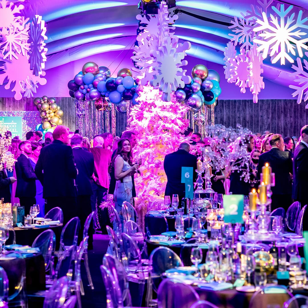 A vibrant gala dinner with guests seated at tables, under a ceiling decorated with crystal ornaments and festive lighting.