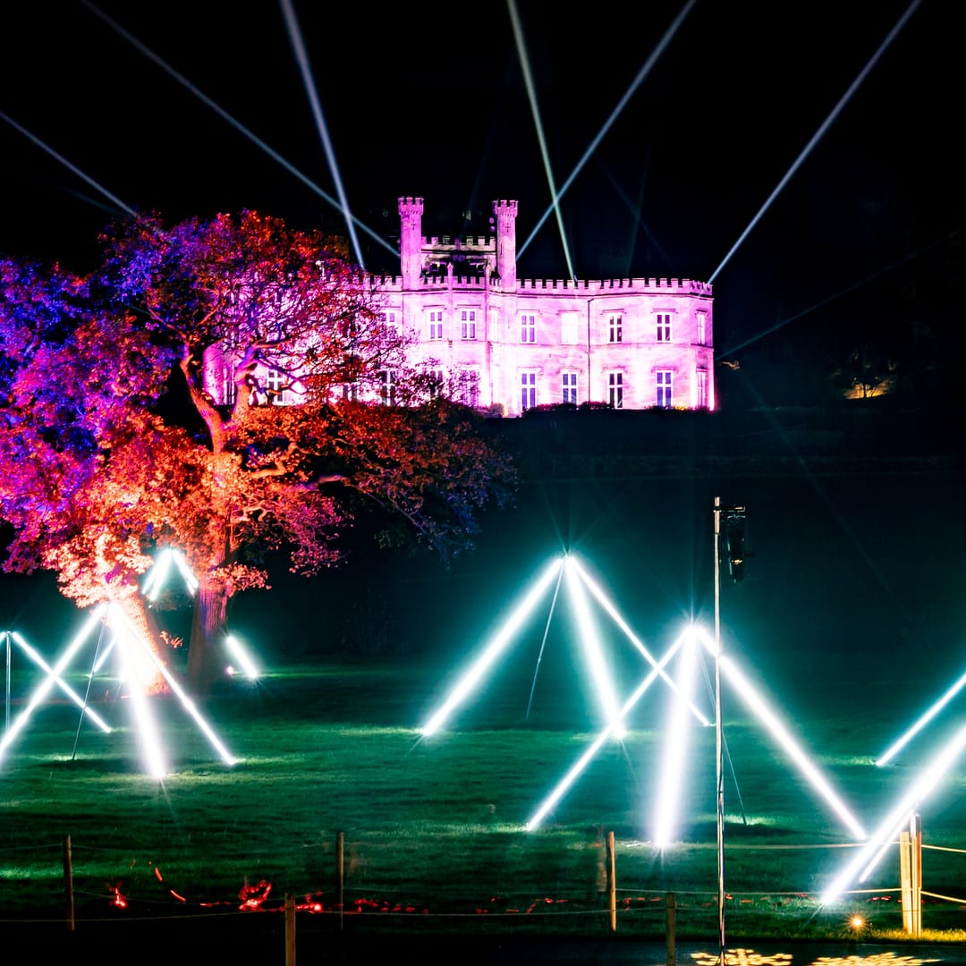 Bolesworth Castle illuminated with vibrant night lights and laser displays, set against a dark evening sky