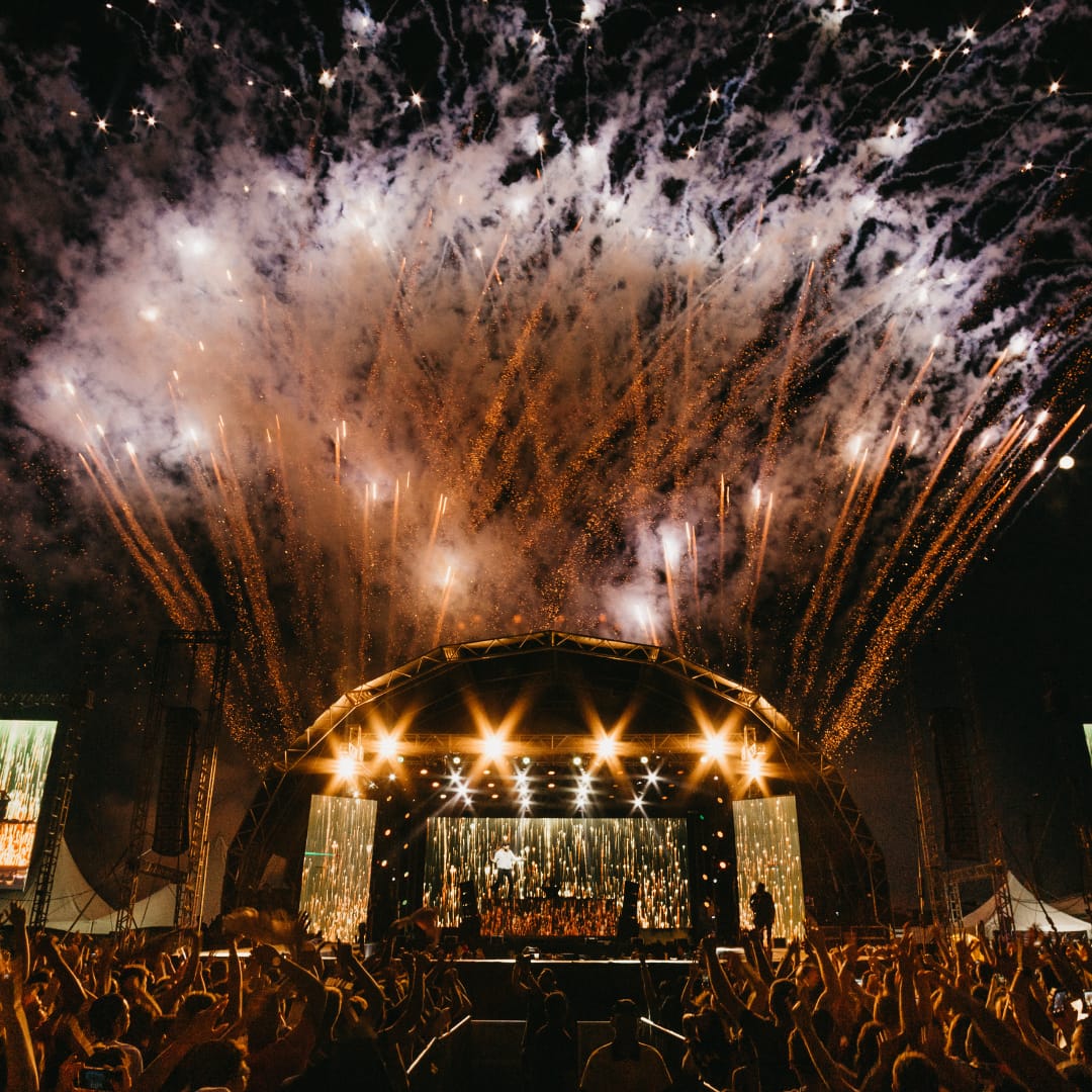 A breathtaking fireworks display erupts over the Together Again Festival main stage, illuminating the night sky as the crowd cheers in celebration.