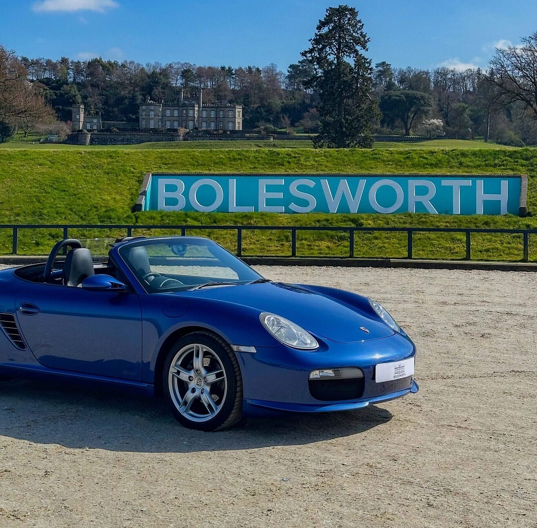 Blue Porche supercar parked in front of a Bolesworth sign with the backdrop of Bolesworth castle in the distance