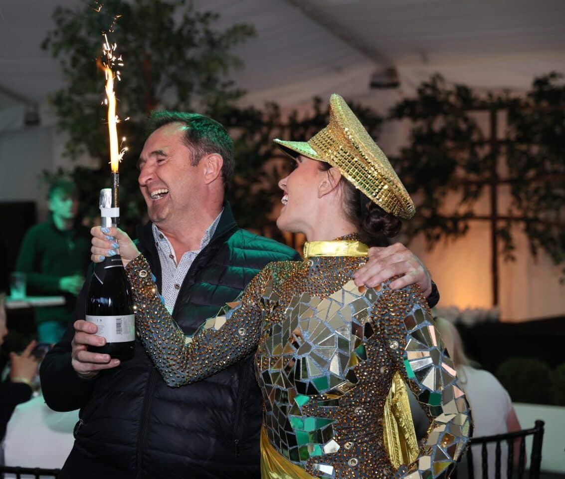 A celebratory moment at Bolesworth Elite Auctions, as a winning bidder receives a bottle of champagne with a sparkler, joined by a performer in a gold mirror outfit.