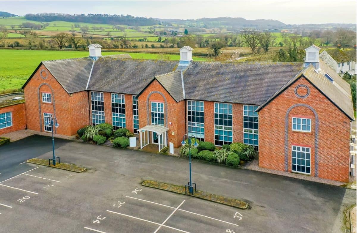 Exterior view of an office at Chowley Business Park featuring brick architecture with large windows, surrounded by scenic countryside.