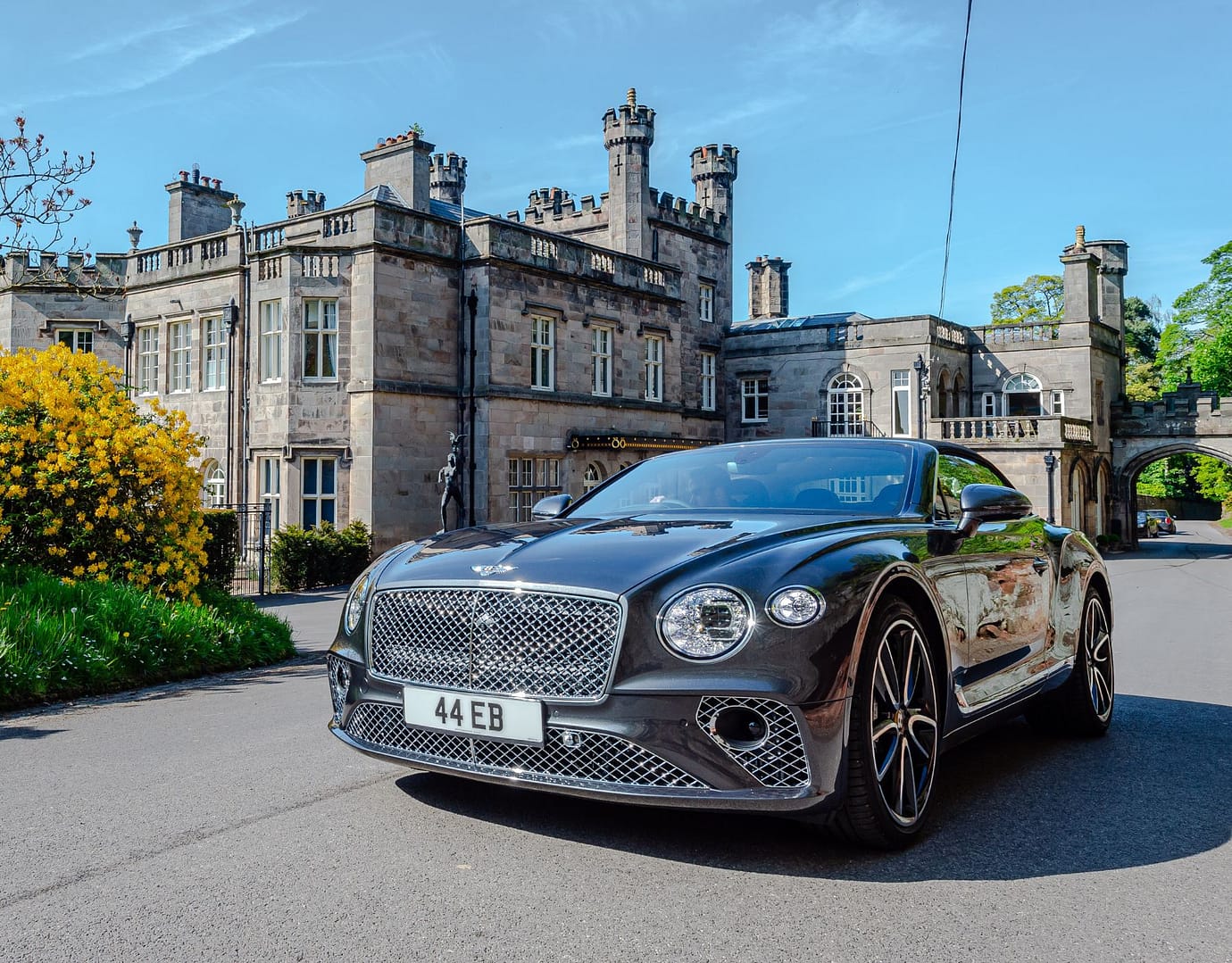 A luxury car parked in front of Bolesworth Castle on a sunny day, showcasing the castle's grand architecture.