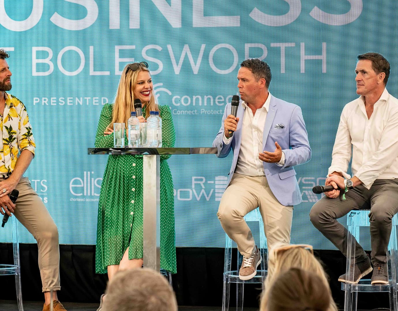 Three business professionals engaging in a panel discussion on stage, with a branded backdrop behind them.