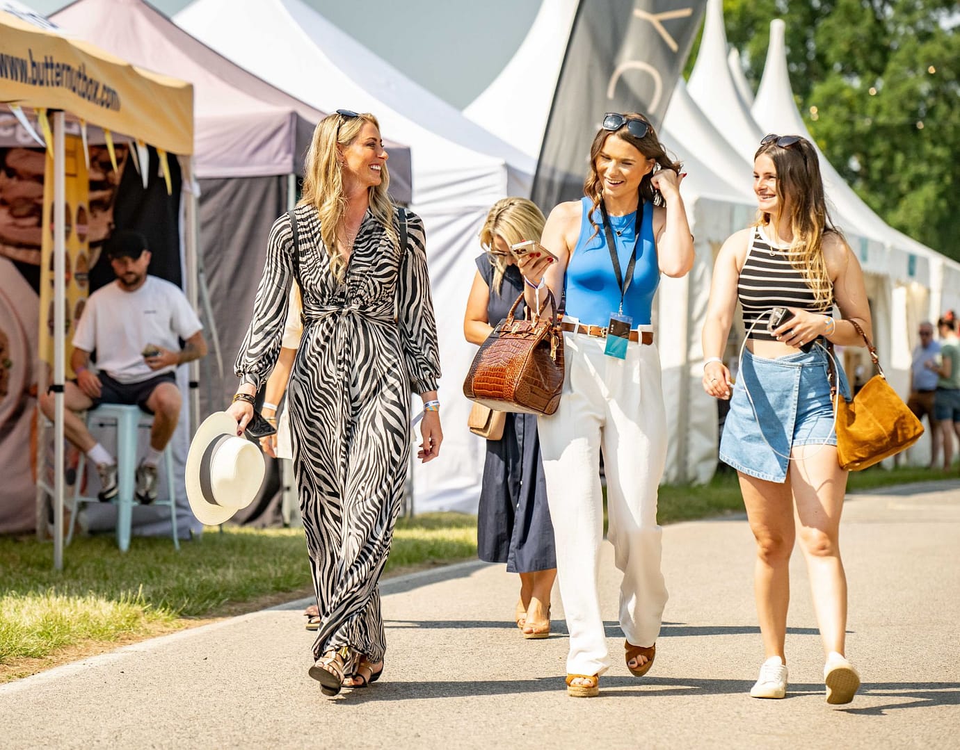 Three fashionable women walking through the vibrant Bolesworth International event, surrounded by white tents and festival energy.