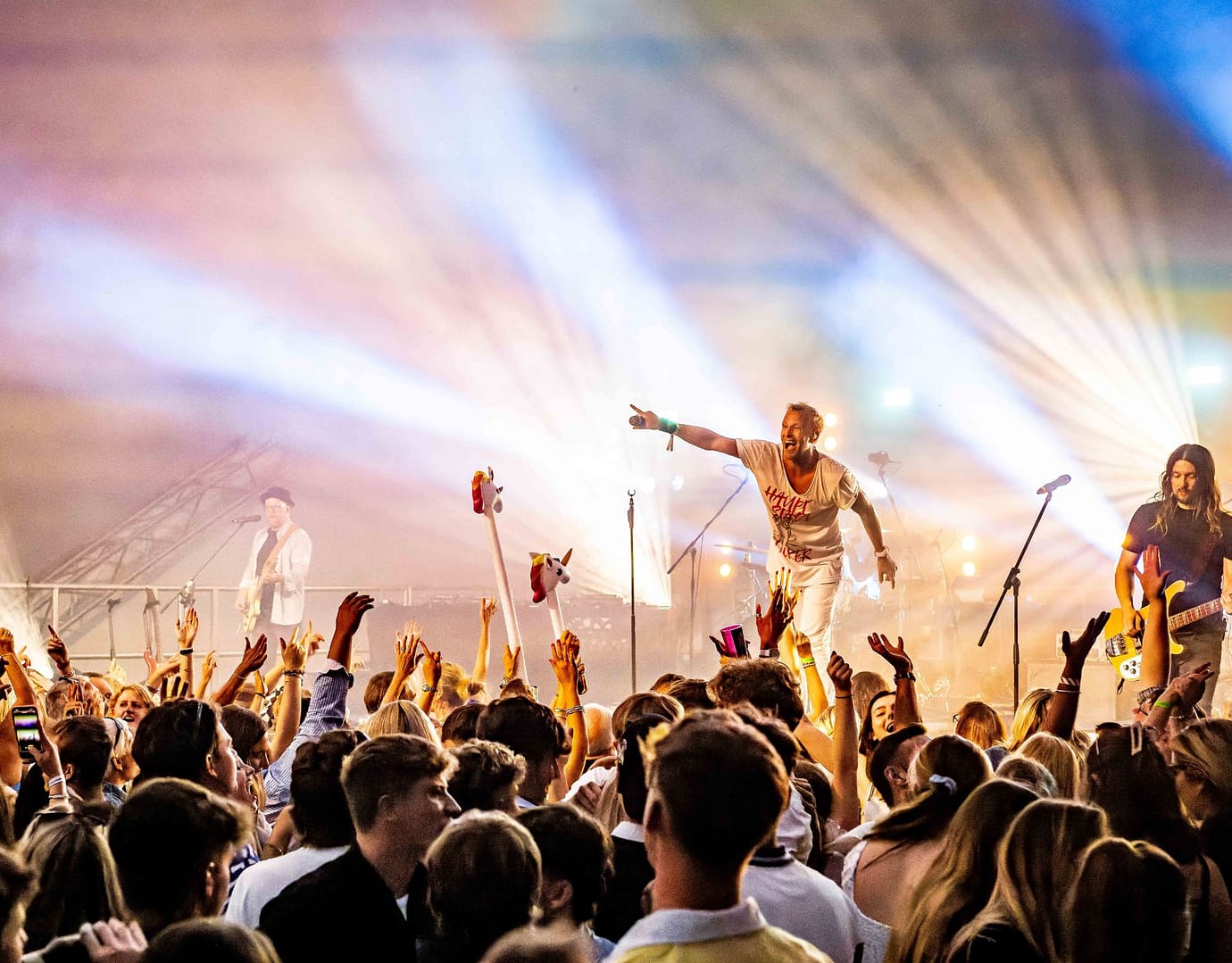 Excited crowd at a live concert with vibrant stage lights and performers engaging the audience.