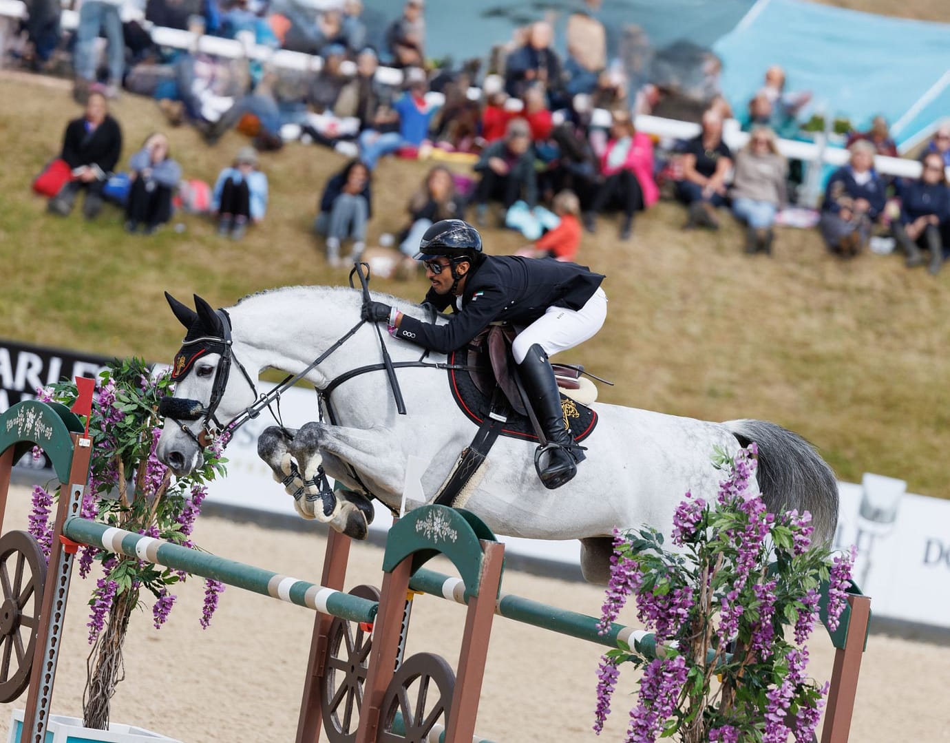 Al Shiraa showjumping rider clears a jump at Bolesworth International Horse Show, with a focused crowd watching in the background.