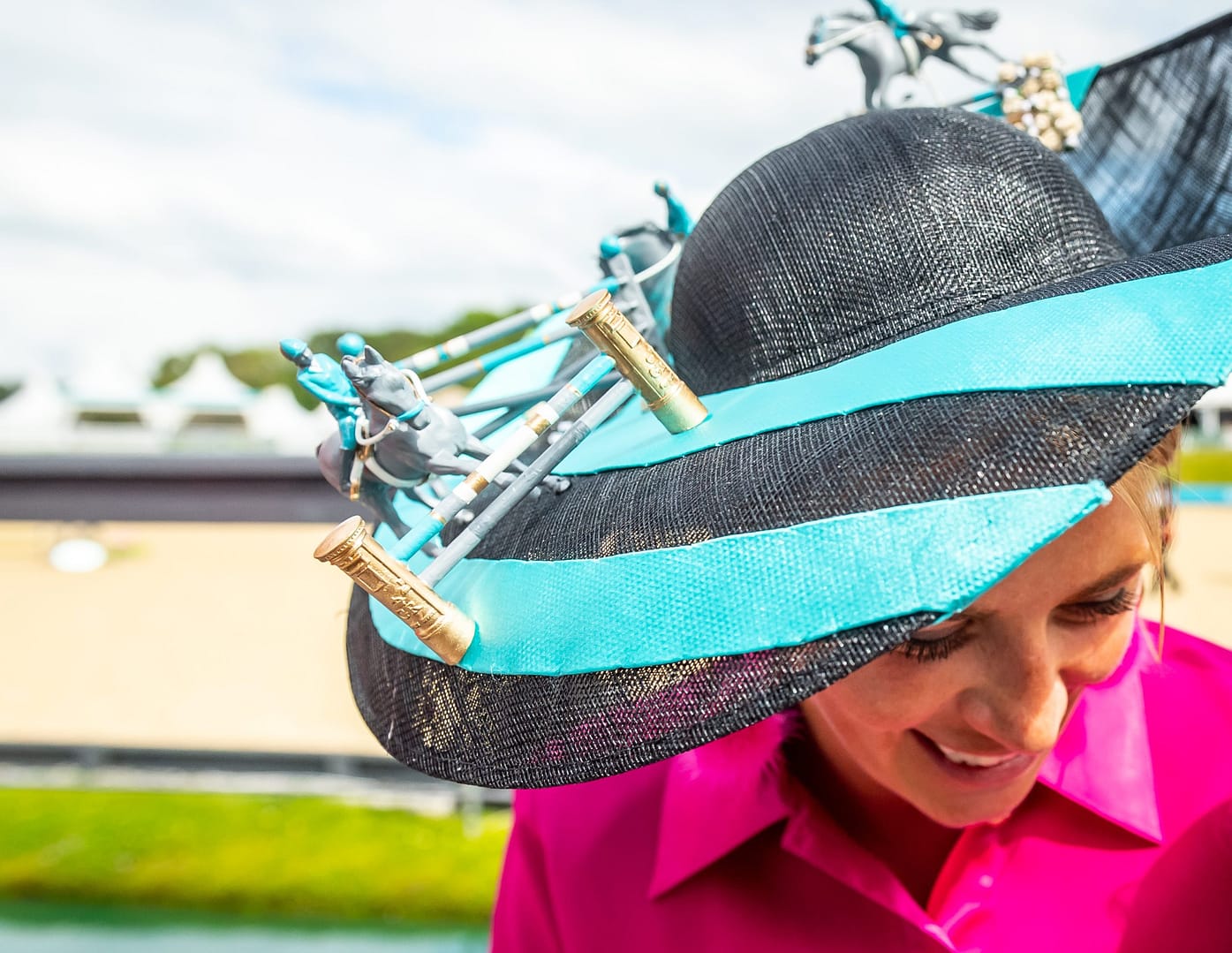 A close-up of a woman wearing a striking black and turquoise hat adorned with miniature horse and rider figurines, attending the Bolesworth International event.