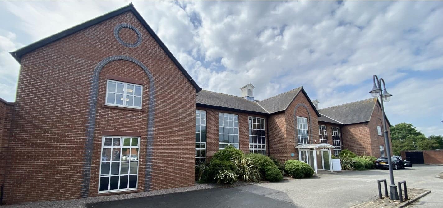 A modern two-story brick office building with large windows, dedicated parking, and landscaped surroundings at Chowley Oak Business Park, Cheshire. The property features spacious office suites, natural light, and excellent transport links for businesses looking for a strategic location.