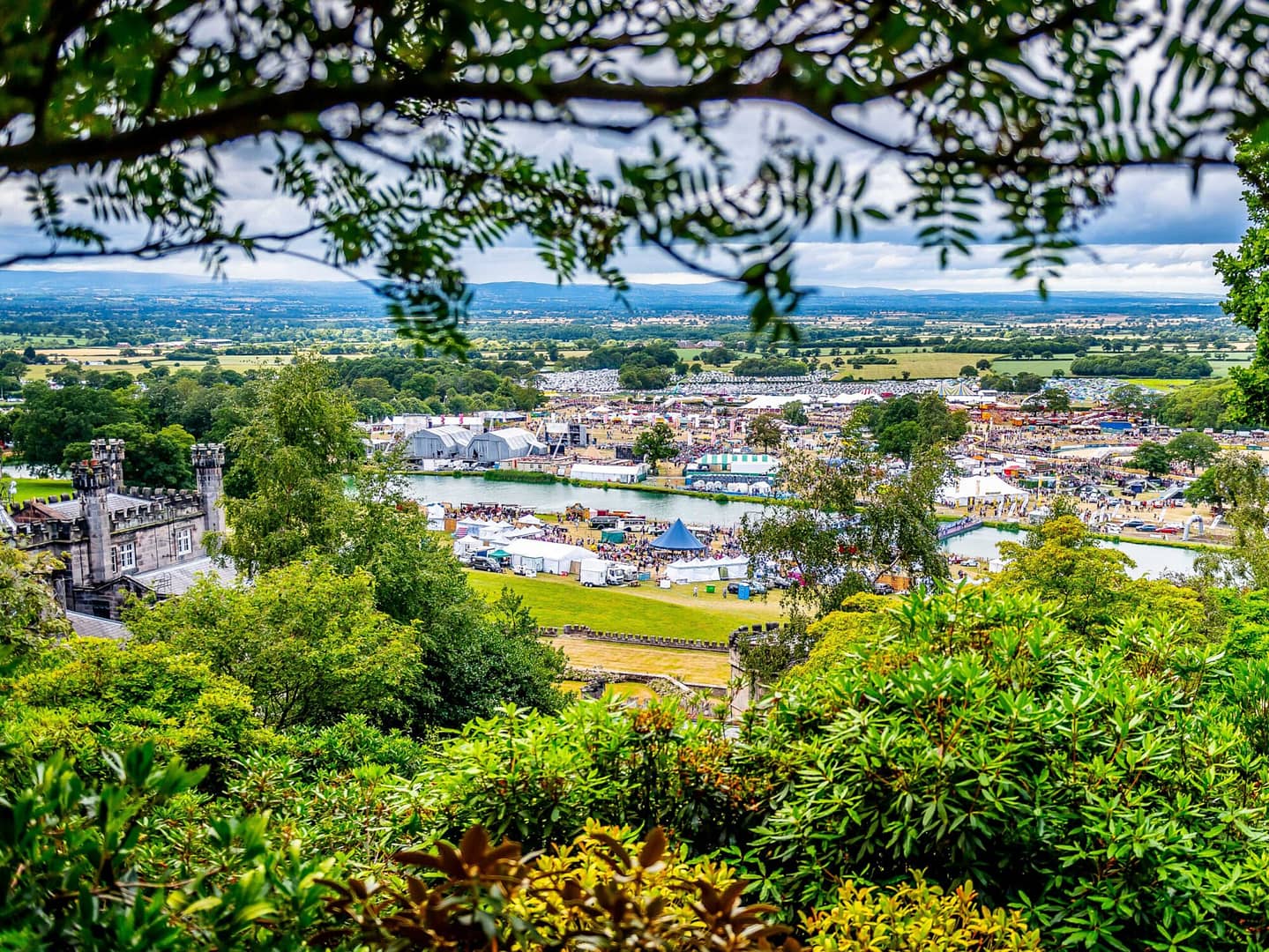 A vibrant aerial view of a festival at Bolesworth, showcasing the event site, historic estate, and scenic Cheshire countryside.