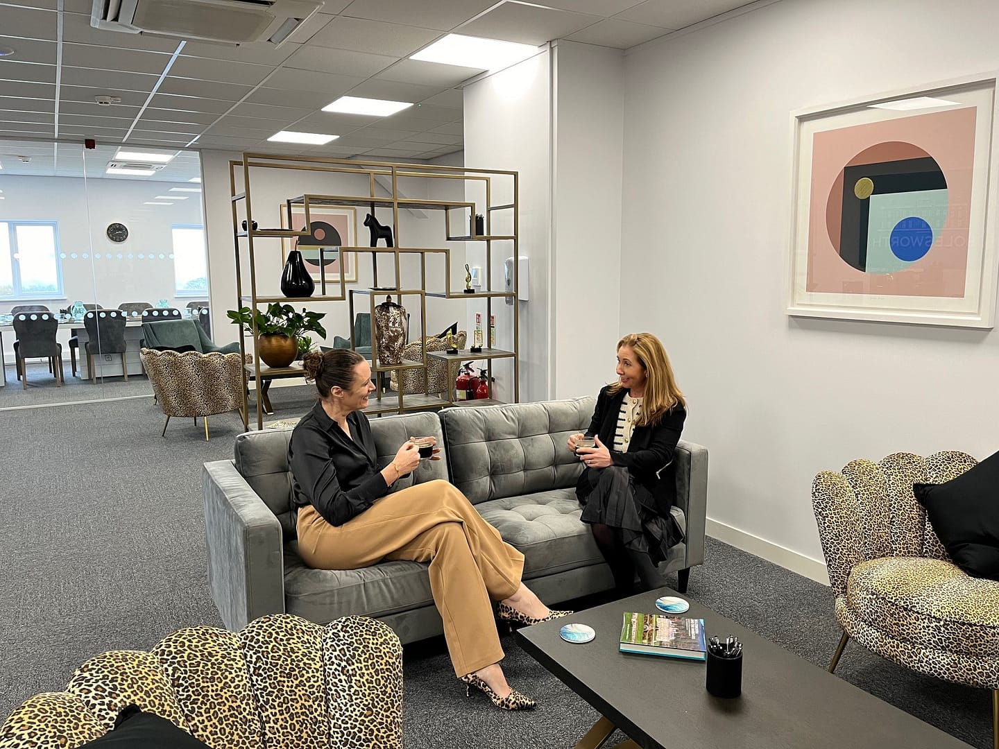 Two business women sitting down on a sofa chatting in an open plan meeting space