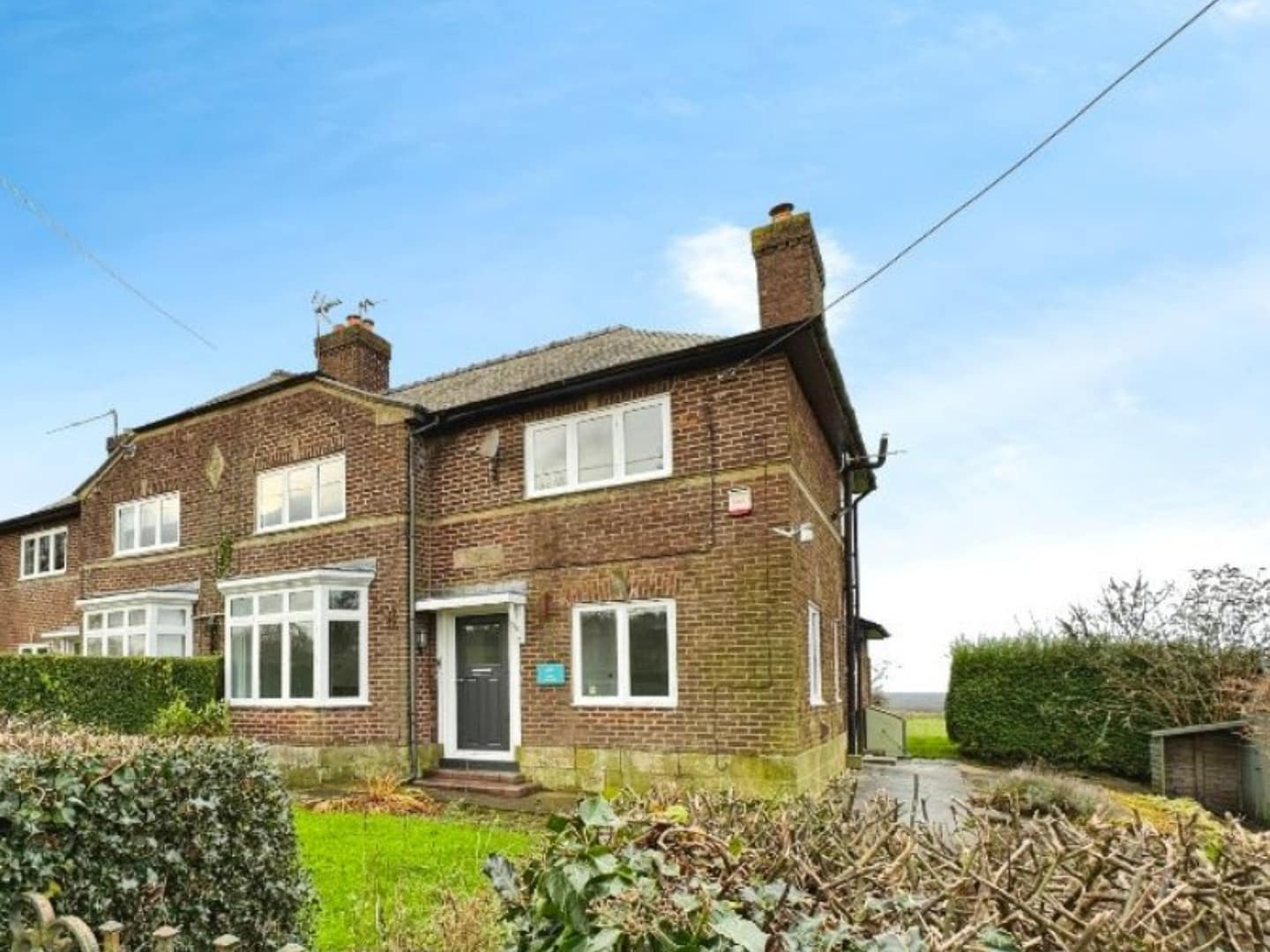 A charming semi-detached brick-built cottage, featuring bay windows, a modern entrance door, and a spacious garden, with beautiful countryside views in the background.