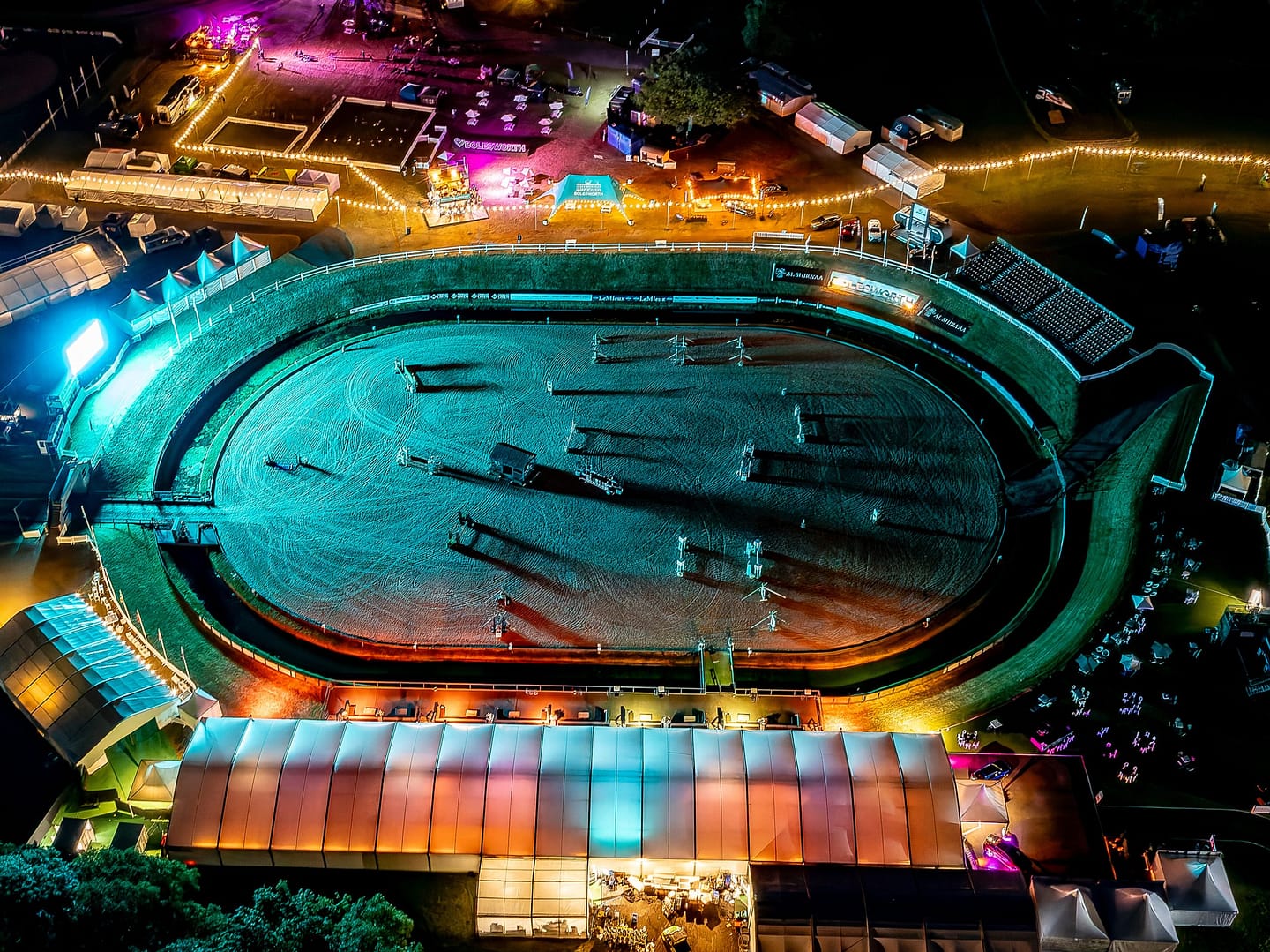 Night-time aerial view of the Bolesworth International Arena, brightly lit with colourful lights, surrounded by event structures and activities.
