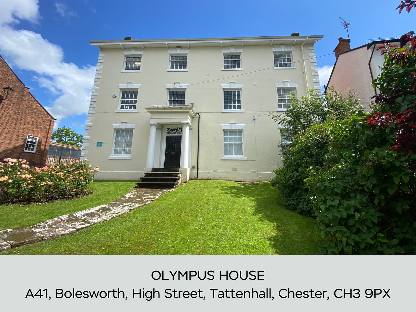 A grand three-story Georgian-style office building, Olympus House, with a cream façade, symmetrical sash windows, and a classic portico entrance. The property is surrounded by lush greenery, a manicured lawn, and a stone pathway leading to the entrance. Located at A41, High Street, Bolesworth, Tattenhall, Chester, CH3 9PX.