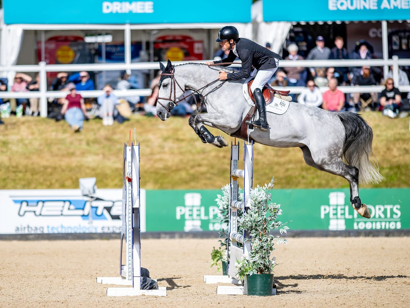 Horse and rider clearing a jump during Bolesworth International, with Peel Logistics and Helite branding visible in the background.