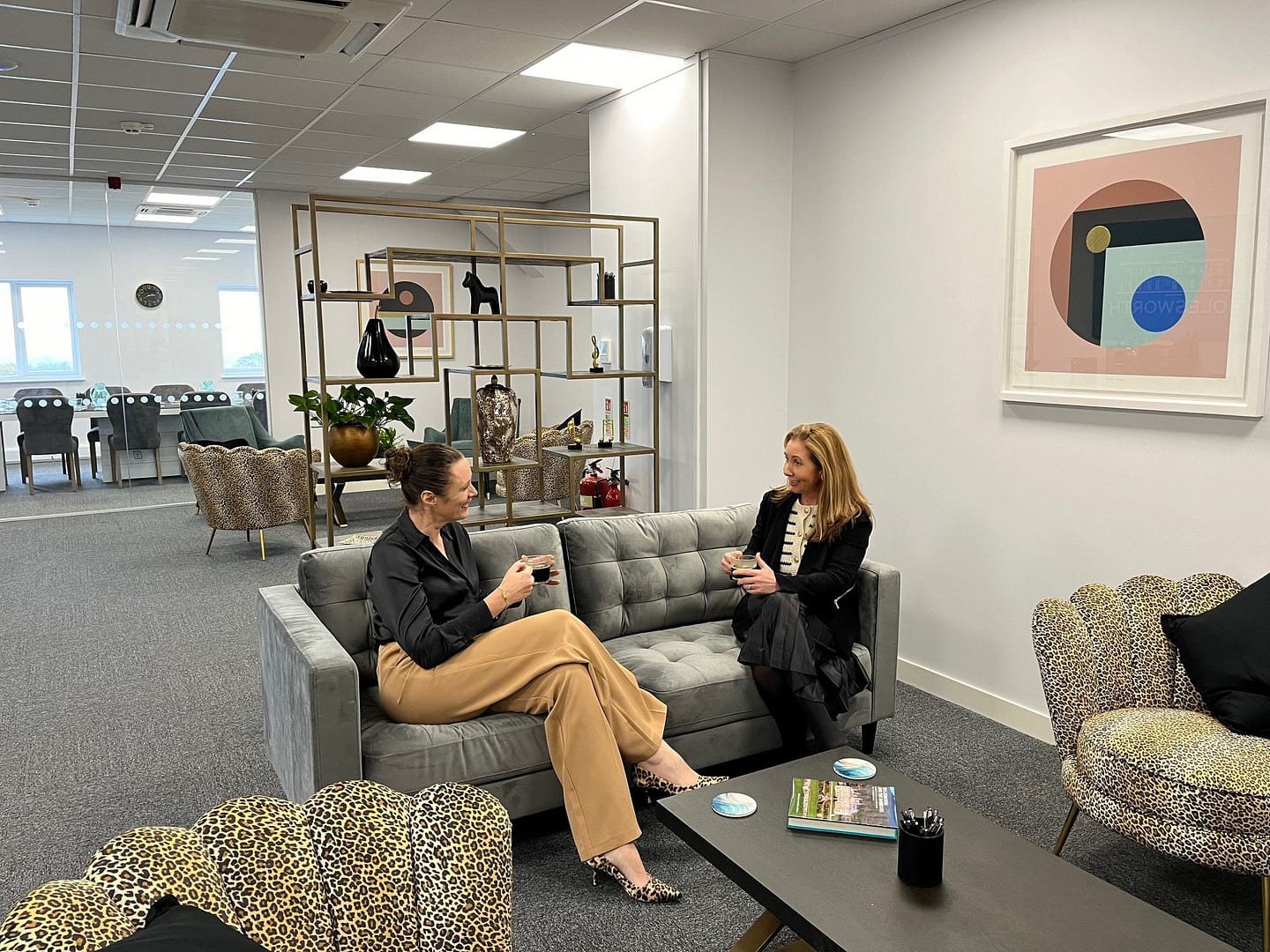 Two business women sitting down on a sofa chatting in an open plan meeting space