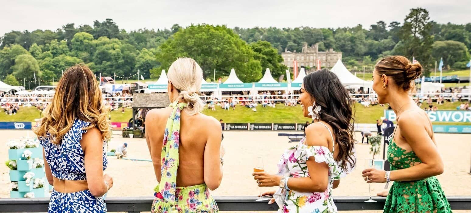 Four elegantly dressed women standing on a terrace, overlooking the Bolesworth show ground during Ladies Day.