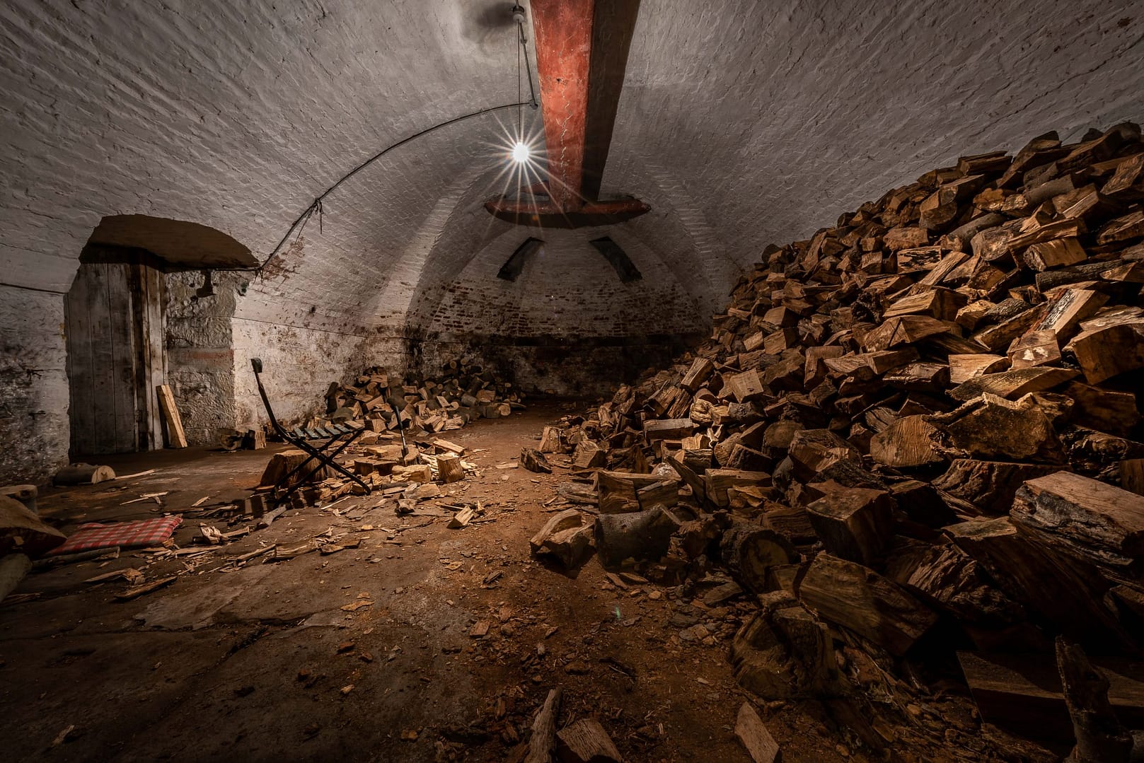 A rustic underground cellar at Bolesworth Estate, featuring vaulted brick ceilings, weathered stone walls, and an expansive woodpile. The dimly lit space, illuminated by a single hanging light, adds an atmospheric, cinematic quality, making it an ideal setting for film productions, historical documentaries, and photography projects.