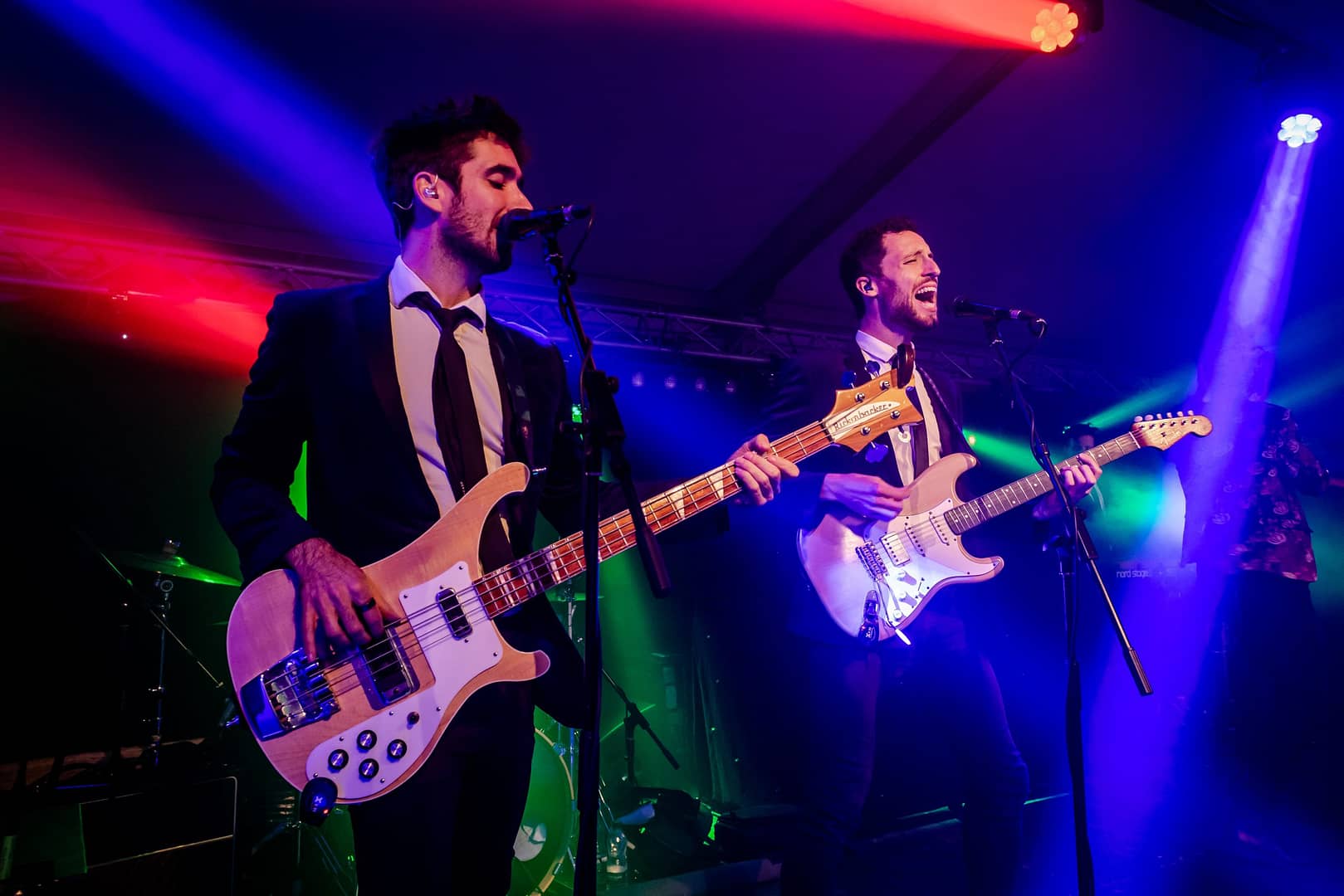 A live band performing at Bolesworth International Horse Show’s nightlife event, featuring two musicians in black suits playing guitars under vibrant stage lighting.