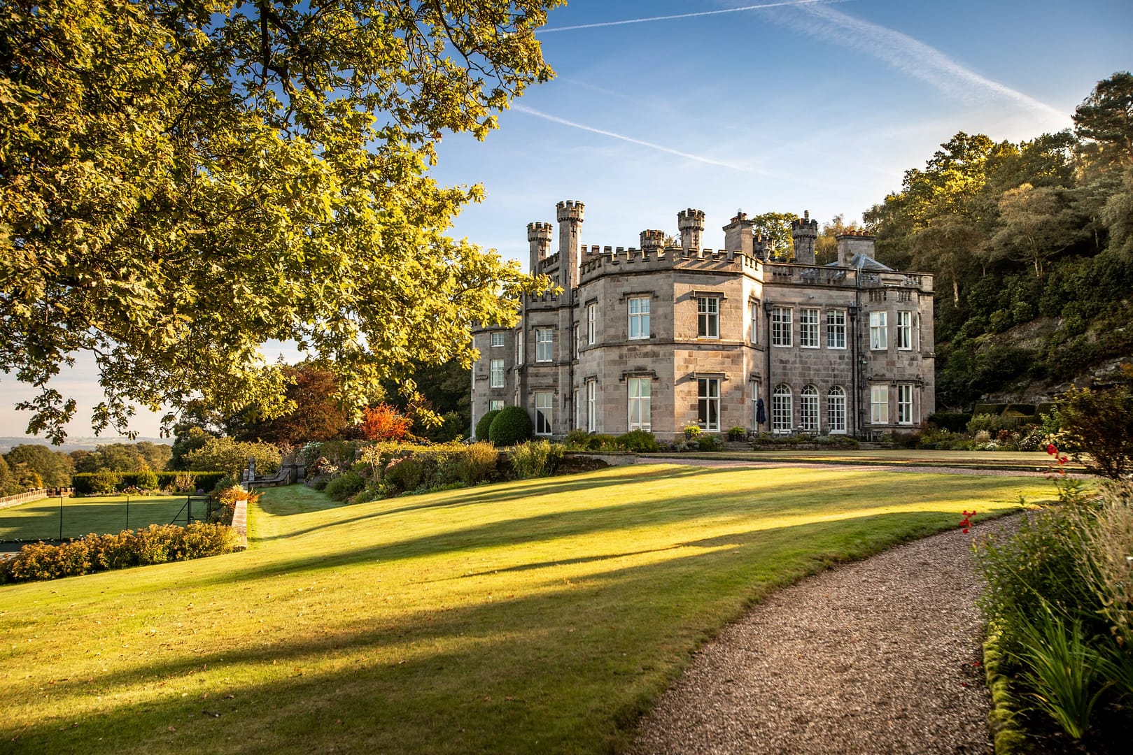 A breathtaking view of Bolesworth Estate, a historic country house set amid rolling green lawns and picturesque gardens, bathed in golden sunlight.