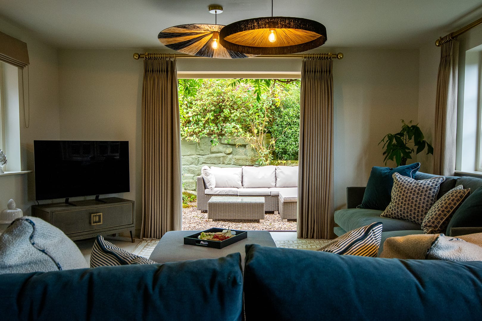 Sitting room with 2 larges sofas and a TV with patio doors open with rattan chairs and coffee table