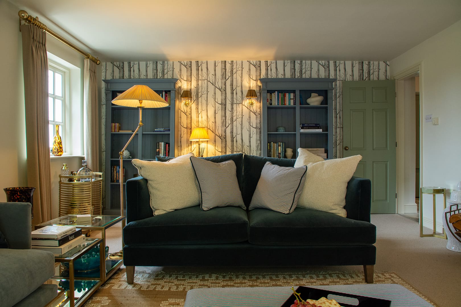 Sitting Room with large compfy sofa with scatter cushios, free standing lamp and bookshelves behind.