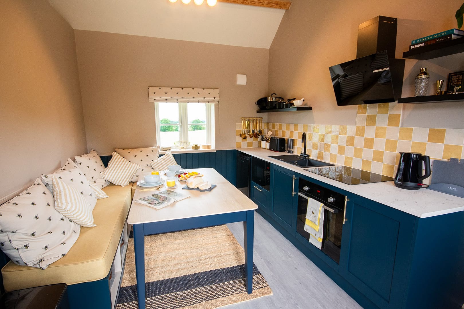 Kitchen diner with blue kitchen cupboards and small table and bench seating with a small window.