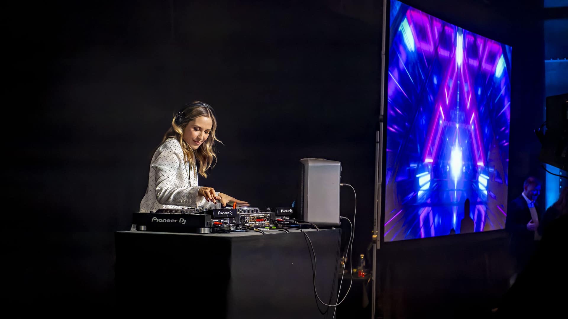A female DJ performing live at the Bolesworth Elite Auction 2024, captivating the audience with an immersive sound experience. The image showcases a vibrant digital display, professional DJ equipment, and a high-energy atmosphere.