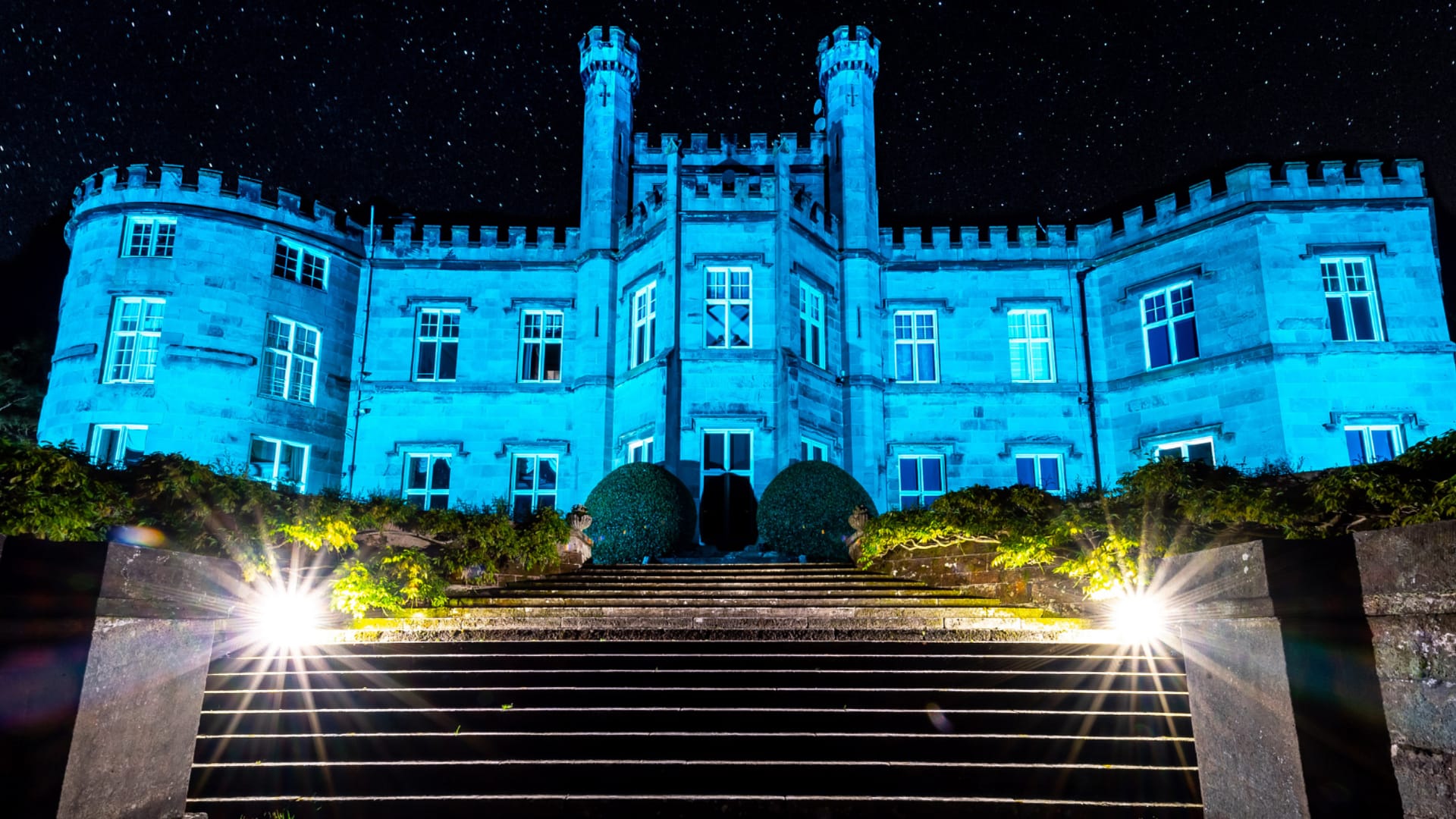 Bolesworth Castle illuminated in blue light at night with steps leading up to the entrance.
