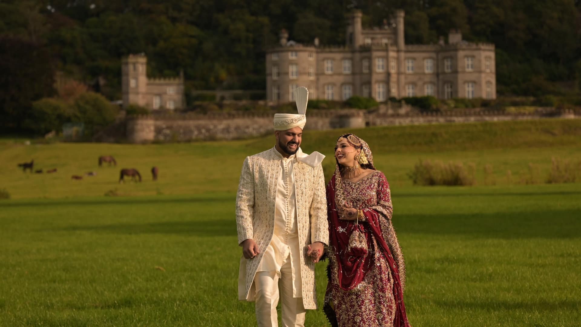 Couple in traditional wedding attire walking on the lawn in front of Bolesworth Estate.