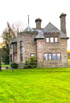 Liongate Lodge exterior, a charming stone building with a well-kept lawn and lush greenery.