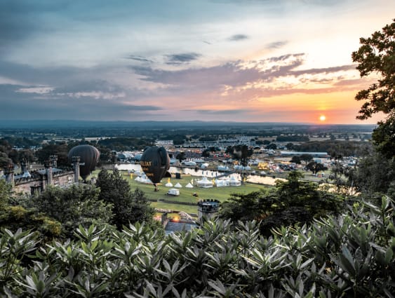 Aerial view of festival grounds at Bolesworth with air balloons and tents set up on the grounds with the sunset