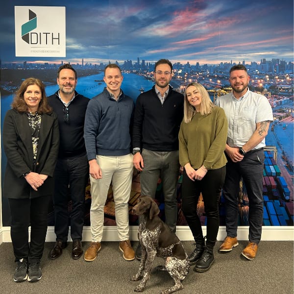 Duferco UK team posing at Chowley Business Park, with a company logo and a friendly office dog.