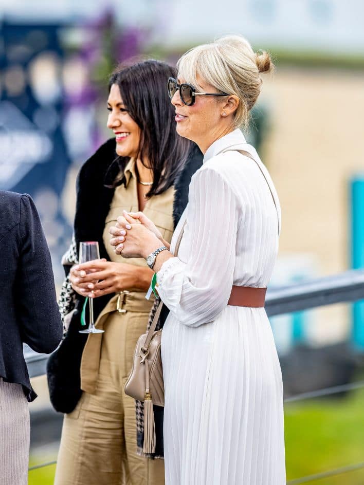 Two women standing looking out onto the show ground, chatting and sipping champagne.