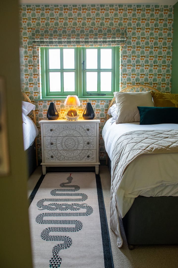 Twin bedroom with beds either side of a window and set of drawers.