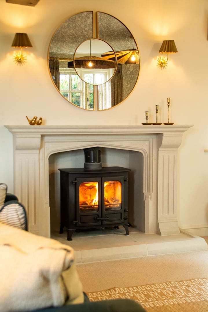 A fireplace with a Log burner with two wall lights either side a large circular mirror