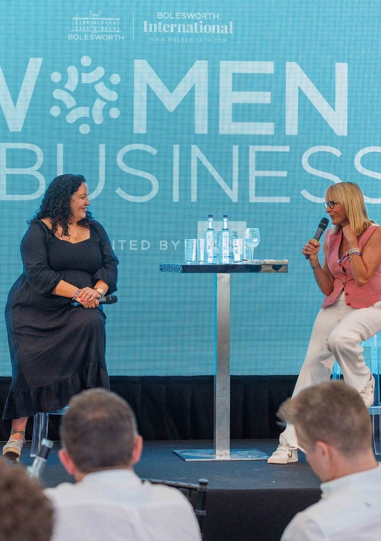 Three women seated on a stage engage in a discussion during a Women in Business panel, with a Bolesworth backdrop in view.