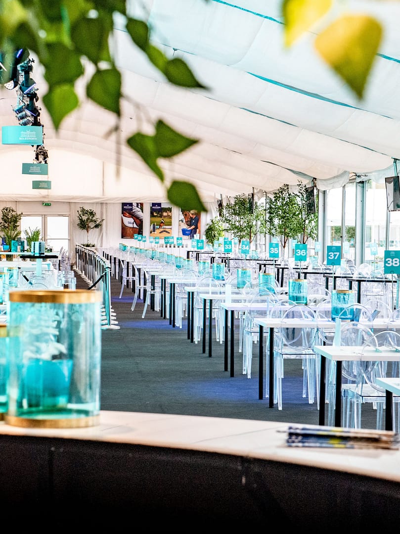Interior of the Bolesworth hospitality marquee featuring elegant modern high tables with teal number placements, lush green plants.