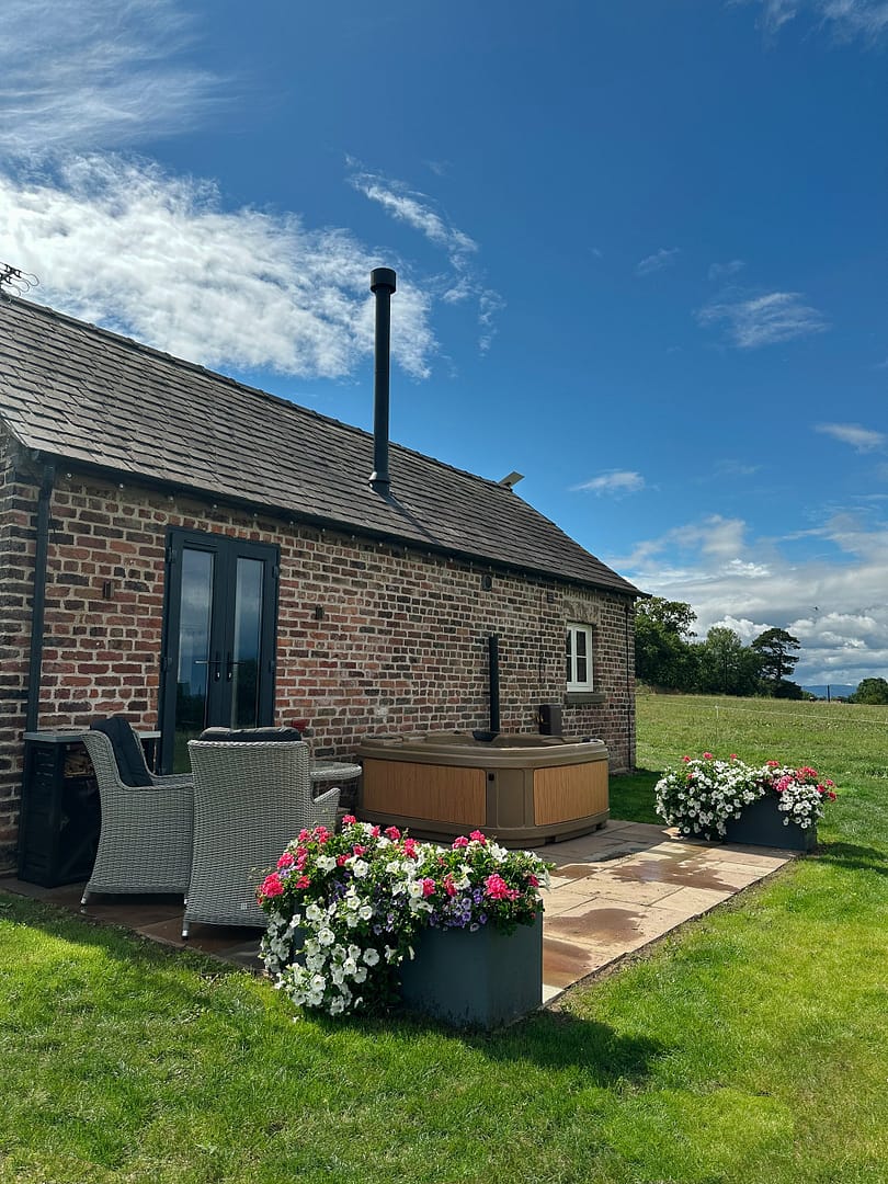 A hot tub located in a garden surrounded by fields with a small table and chairs on the terrace