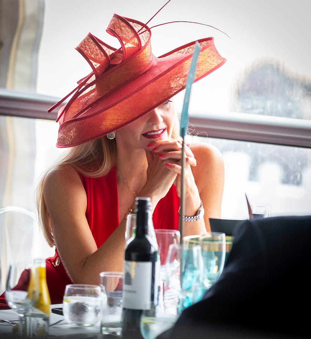 A lady in conversation at a table in the Bolesworth marquee, wearing a red hat and dress.